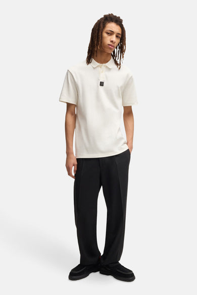 Ecru polo met korte mouwen van HUGO, gedragen met zwarte pantalon en loafer schoenen.