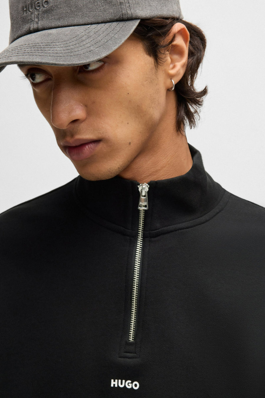 Man met grijze Hugo pet en zwarte trui met ritssluiting.

