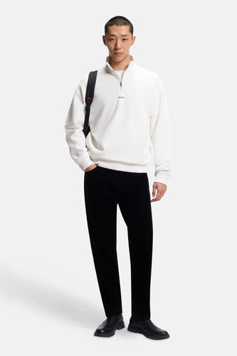 Pull-over blanc à col montant de HUGO, porté avec un sac à dos noir sur un épaule sur une pantalon et des chaussures noirs.