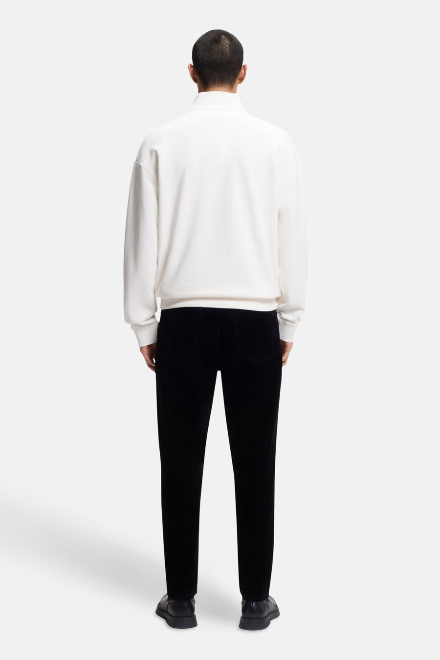 Achterkant van een man in een witte trui en zwarte broek.