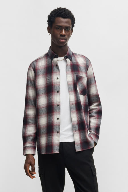 Chemise rouge à manches longues de HUGO, avec un motif à carreaux, portée sur un T-shirt blanc et un pantalon noir.