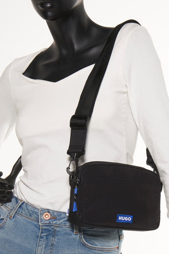 Sac à dos noir HUGO BLUE, avec des bretelles ajustables et des accents bleus, porté par un mannequin en jeans et chemise blanche.