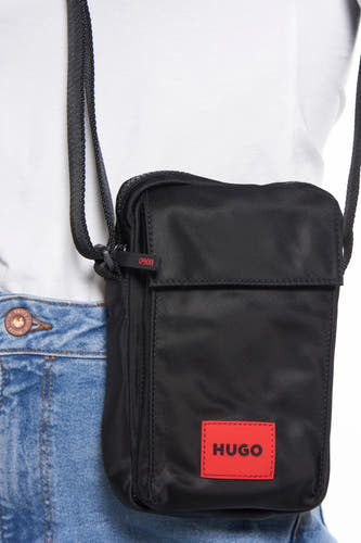 Sac à dos noir HUGO, avec patch de logo rouge, porté sur un t-shirt blanc et des jeans.