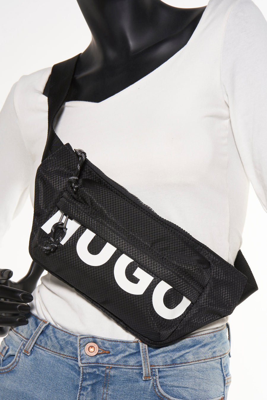 Sac à dos noir HUGO, avec un motif de carreaux et des lettres de marque blanches, porté sur une chemise blanche et un jean.