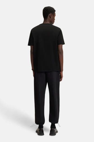 T-shirt noir à manches courtes de HUGO, vu de dos, avec un pantalon noir et des chaussures.