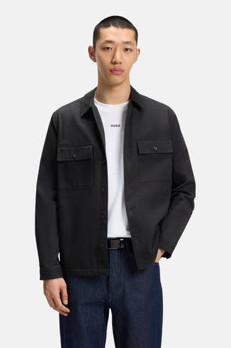 Chemise noire à manches longues de HUGO, avec poches po po et portée sur un T-shirt blanc avec logo et des jeans foncés.