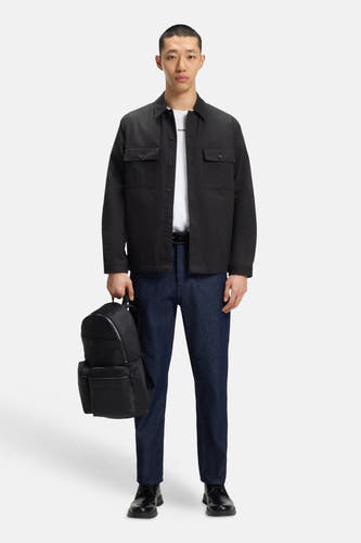 Chemise noire à manches longues de HUGO, portée sur un T-shirt blanc, avec des jeans foncés et une sacoche noire.