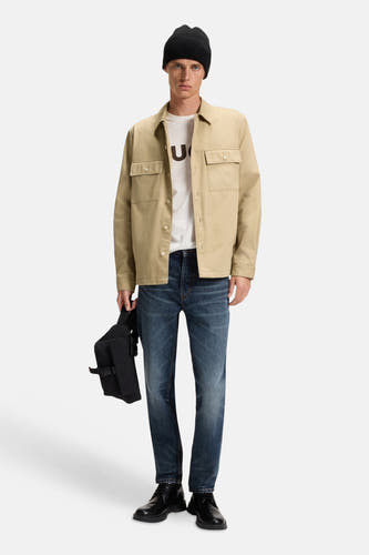 Chemise beige à longues manches de HUGO, portée avec un T-shirt blanc, des jeans bleu marine et un chapeau noir.