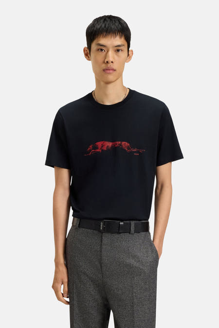 T-shirt noir à manches courtes de HUGO, avec imprimé de chien rouge sur l'avant, associé à un pantalon gris et une ceinture.