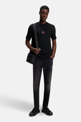T-shirt noir à manches courtes de HUGO, avec une patch logo logo rouge carré, combiné avec un sac à dos noir et des jeans foncés.