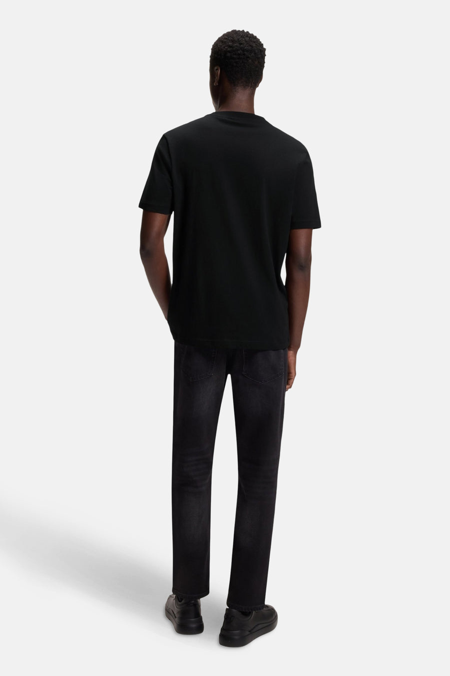 T-shirt noir à manches courtes de HUGO, vu de derrière, avec des jeans foncés et des chaussures noires.