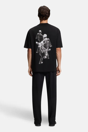 T-shirt noir à manches courtes de HUGO, avec une impression graphique et porté avec un t-shirt à manches longues et un pantalon.