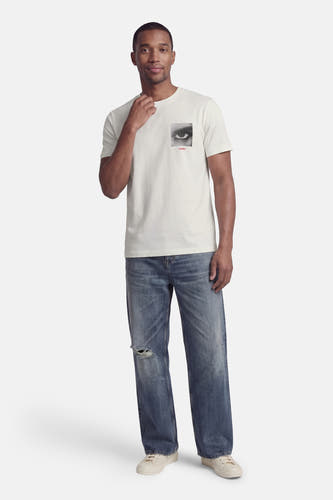 Wit T-shirt met korte mouwen van HUGO, met een zwart-wit oog print op de borst, gedragen met jeans met scheuren.
