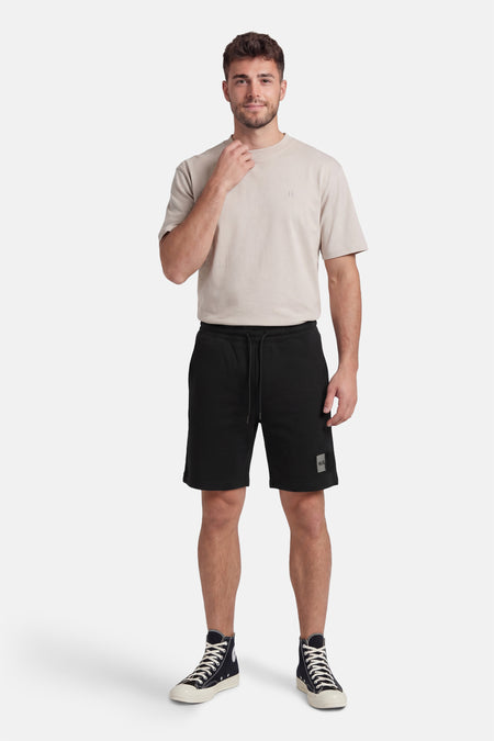 Zwarte short van HUGO, met trekkoord en logo badge op de pijp, gecombineerd met een beige T-shirt en hoge sneakers.
