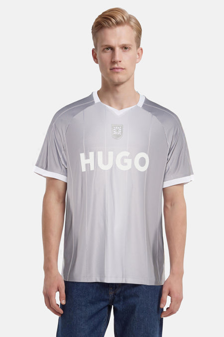 Grijs T-shirt met streepdessin van HUGO, voorzien van witte 'HUGO'-letters en een embleem, gedragen door een man met blauwe jeans.