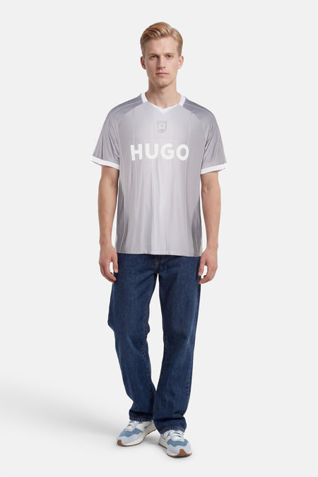 T-shirt gris à rayures diagonales de HUGO, avec logo blanc, écusson, col en V et bords blancs, porté par un homme.