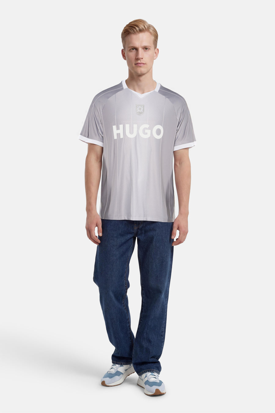 T-shirt gris à rayures diagonales de HUGO, avec logo blanc, écusson, col en V et bords blancs, porté par un homme.