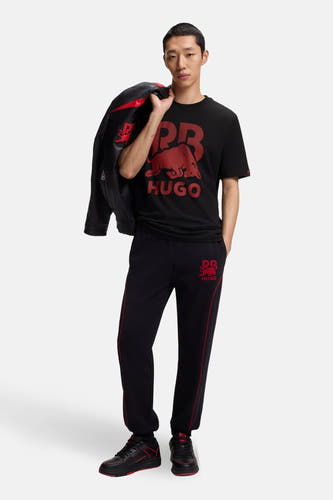 T-shirt noir à manches courtes de HUGO, avec un imprimé rouge sur le devant et un mannequin portant une veste en cuir sur l'épaule.