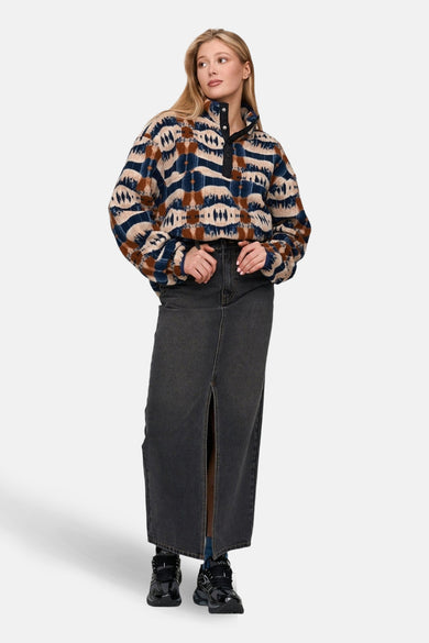 Manteau polaire multicolore de 24 couleurs GMBH avec un motif aztèque, porté avec une longue veste en cuir et des chaussures noires.