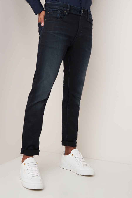 Jean slim bleu marine de G-Star RAW, avec des poches rabattues et associé à des baskets blanches.