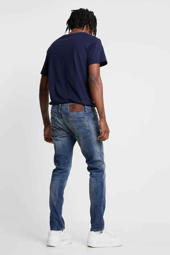Jean slim fit bleu de G-Star RAW, avec un lavage légèrement délavé et des baskets blanches.