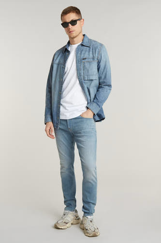 Jean skinny bleu clair de G-Star RAW, porté avec un T-shirt blanc et une chemise en denim, avec des lunettes de soleil.