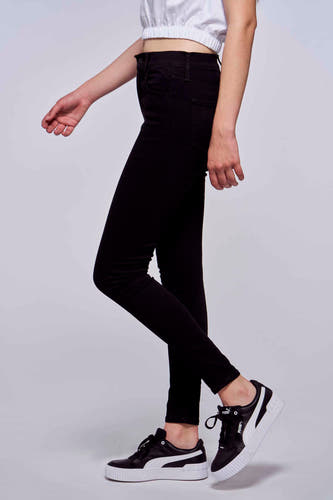 Jean skinny noir de Levi's, porté avec un haut blanc et des baskets noires et blanches, en vue latérale.