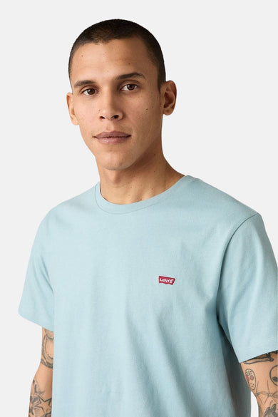 T-shirt bleu à manches courtes de Levi's, avec un petit logo rouge sur la poitrine et des tatouages visibles sur les bras.