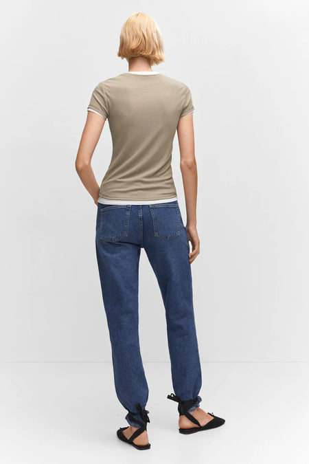 T-shirt à manches courtes vert olive de MANGO, vue de dos, avec liseré blanc au col et aux manches, porté avec un jean bleu et des sandales noires.