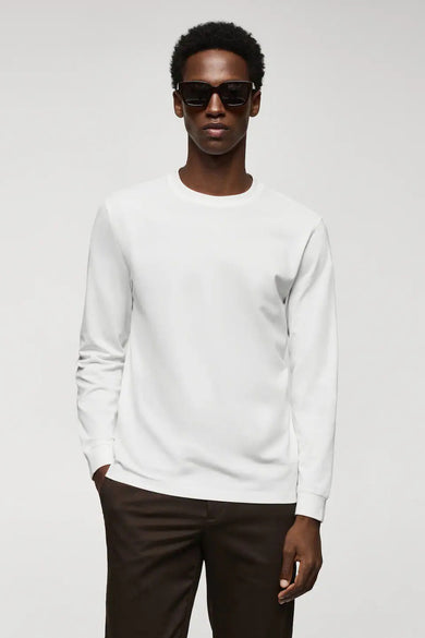 T-shirt blanc à manches longues de MANGO, design simple avec col rond, porté par un mannequin avec un pantalon foncé et des lunettes de soleil, vue de face