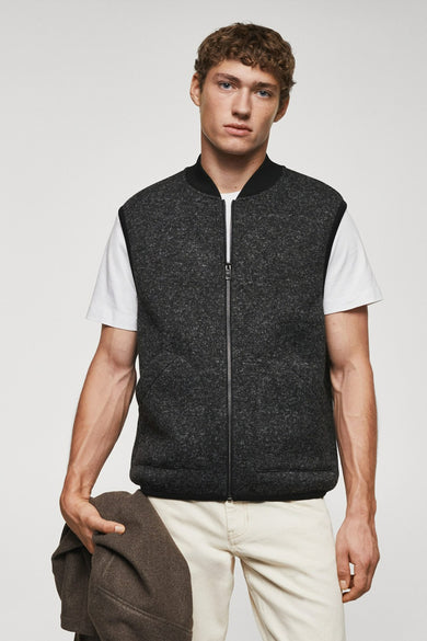 Gilet gris de MANGO, porté sur un T-shirt blanc et une veste brune dans la main.