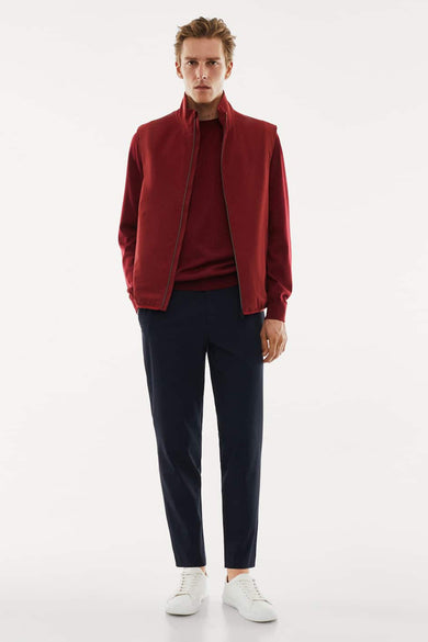 Gilet rouge de MANGO porté sur une chemise rouge avec un pantalon bleu marine et des baskets blanches.