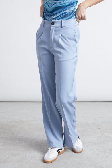 Pantalon bleu de 24 couleurs, avec poches et larges basques, associé à des sneakers blanches.