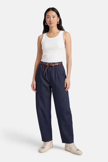 Mom jeans en denim bleu foncé de Terra di Siena, avec une ceinture marron, combinées avec un débardeur blanc et des baskets couleur crème.