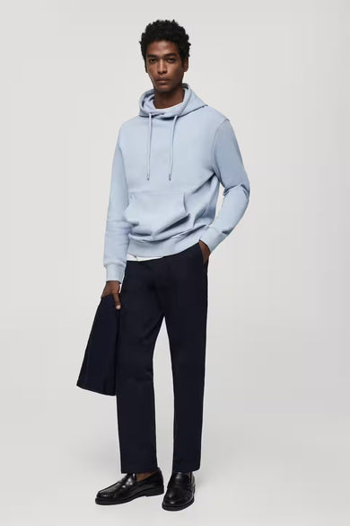 Pull-over bleu avec capuche de MANGO, associé à un pantalon foncé et des chaussures en cuir.