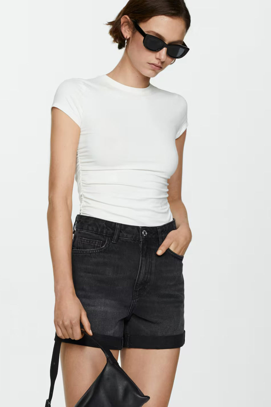 Short de denim noir de MANGO, avec des pinces relevées et une femme avec un chapeau de soleil et une chemise blanche.