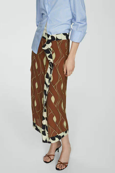 Jupe brune de MANGO avec un motif ondulé frappant et des détails noirs et blancs sur les côtés, associée à une chemise bleue rayée.