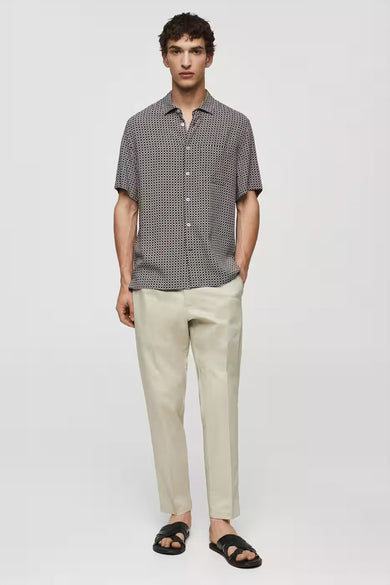 Chemise bleue à manches courtes de MANGO, avec un motif géométrique, associée à un pantalon beige et des sandales noires.