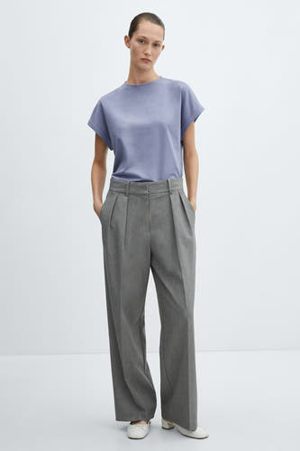 T-shirt bleu à manches courtes de MANGO, stylisé avec un pantalon gris plissé et des mules blanches.