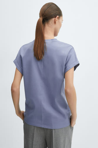 Blauw T-shirt van MANGO, achterkant van model met korte omgeslagen mouwen, verticale naad op de rug en grijze broek.