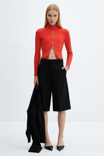 Veste rouge de MANGO, avec des manches longues et une fermeture éclair, portée avec des culottes noires et des escarpins.