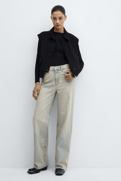 Jean ample en denim de couleur claire de MANGO, porté par un mannequin avec un haut noir et un cardigan, avec des ourlets effilochés et des chaussures noires.
