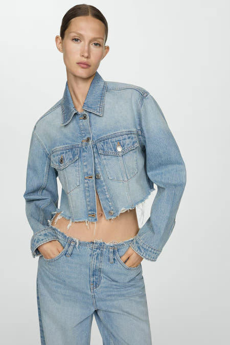 Veste en denim bleu marine de MANGO, portée avec un soutien-gorge noir et des jeans larges dans une position assise décontractée.