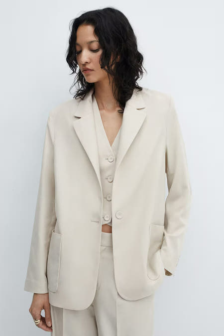 Blazer gris de MANGO, vu de l'rière avec des long long et et une coupe décontractée, associé à un pantalon de la même couleur.