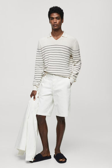 Shorts en denim blanc de MANGO, associés à une chemise rayée et des sandales, avec un manteau dans la main.