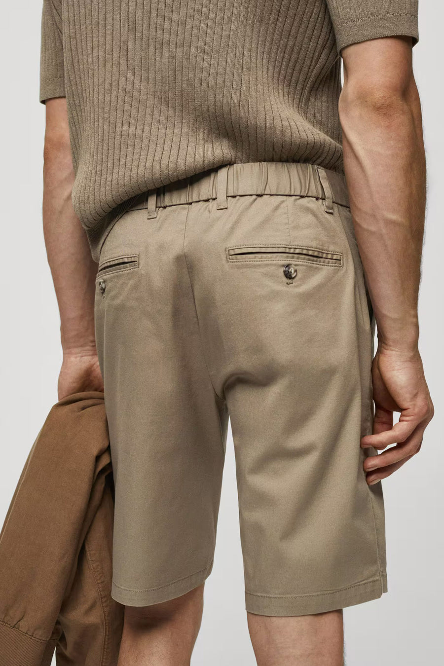 Short marron de MANGO, avec une ceinture élastique et des poches à l'arrière, maintenu par un blouson sur le côté, vue arrière.