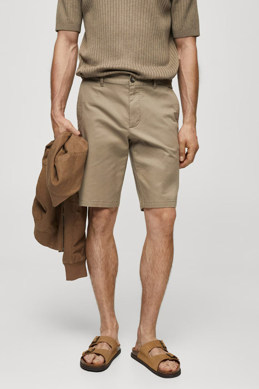 Short marron de MANGO, porté avec des sandales marrons et un t-shirt marron, tenant un manteau marron dans la main.