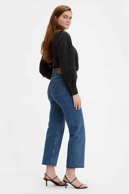 Jean droit en denim bleu moyen de Levi's à taille haute, associé à un chemisier noir et des sandales à talons.