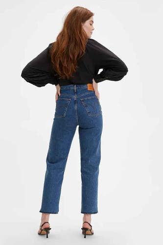 Jean droit en denim bleu moyen de Levi's, avec poches arrière et patch en cuir marron, porté avec un chemisier noir et des talons.