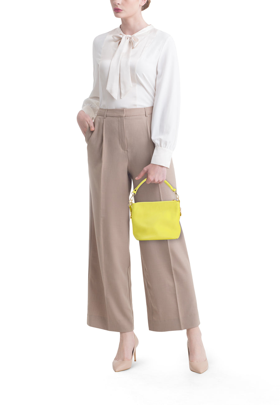 Sac à bandoulière jaune d'Access®, avec texture grainée et ferrures dorées, porté par une femme en pantalon beige.